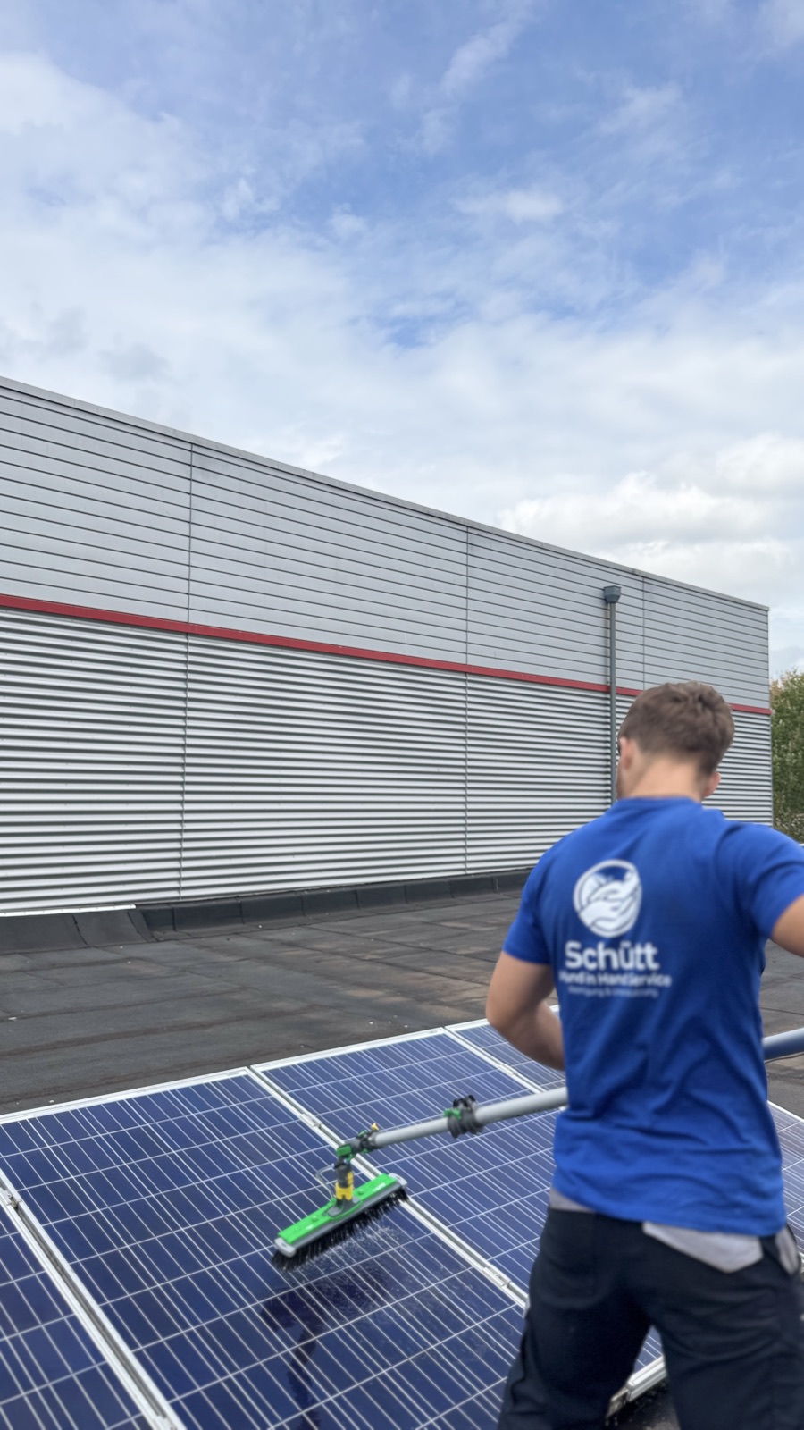 Schütt Hand in Hand reinigt mit der Reinwasser-Bürste ein Solarmodul auf einem Gewerbedach in Bremen